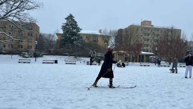 Woman in skis travelling across grass covered in snow