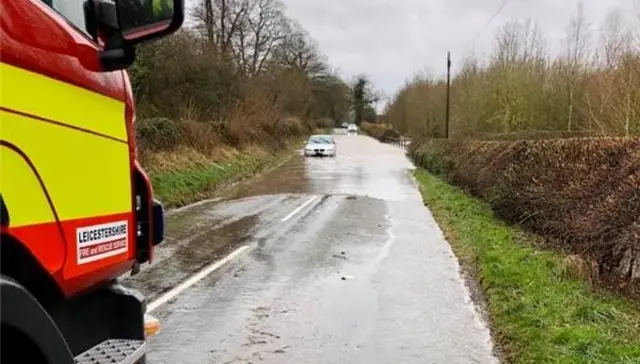 A fire engine parked next to a flooded road with a stranded car