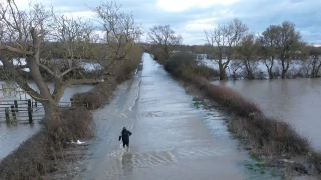 A man wades down a country lane through flood waters.