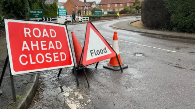 Road closed, flood warning signs, and traffic cones on the village road