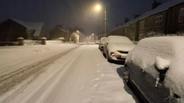 Cars along a road in County Durham are parked and blanketed by snow