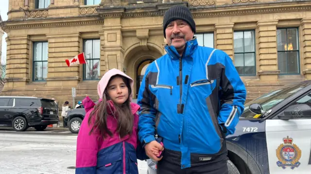 Hames Gamarra stands holding hands with his daughter in front of the PM's office