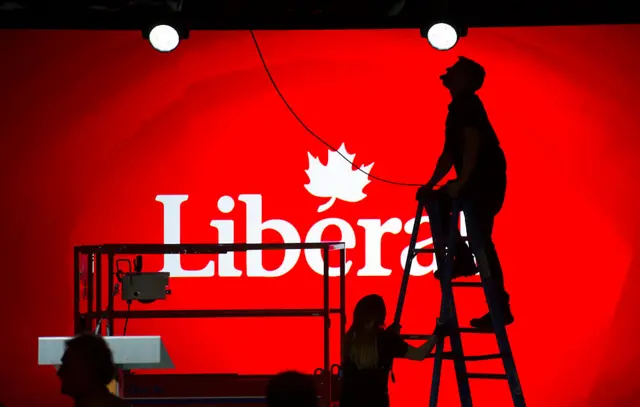 A sign for the Liberal party of Canada is partially obscured by a person on a ladder.