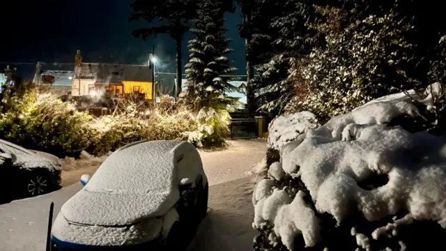 Snow covers a car, hedges and trees in the small Aberdeenshire village of Auchleven