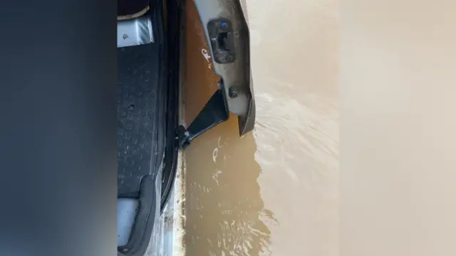 The side of a van in flood water. The door is open and there is brown water up to the bottom of the door.