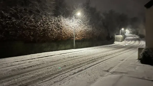 Snowy conditions in Macclesfield, with tyre tracks visible in the twilight