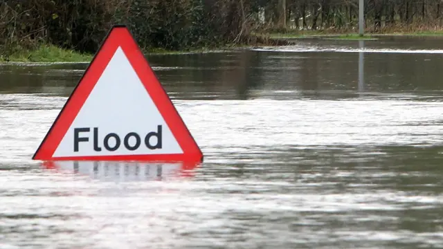 A triangular  flood warning sign partly submerged in a flooded road