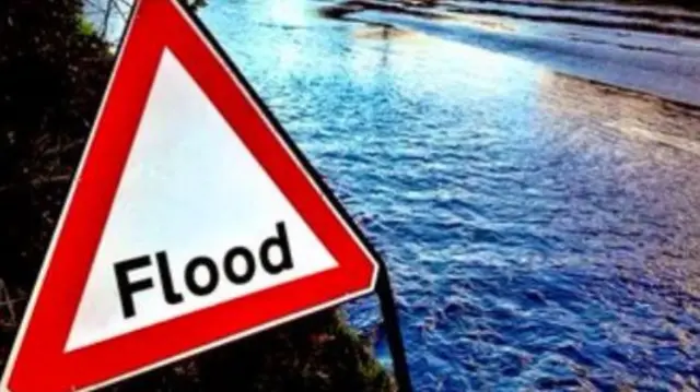 A triangular flood sign in front of a flooded road