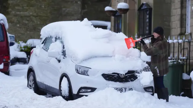 Woman clearing car window of snow using small shovel