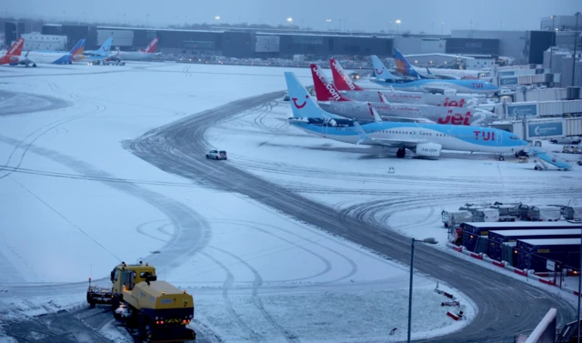 A snow plough waits to help clear snow from around aircraft after overnight snowfall caused the temporary closure of Manchester Airport