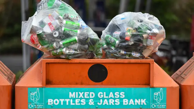 Two bags of beer bottles and cans balanced on an orange skip at a recycling centre