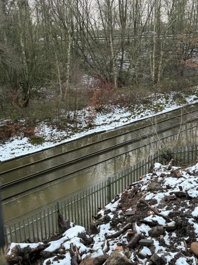 A photograph of flooded railway lines taken from a railway embankment. Snow can be seeneen either side of the tracks