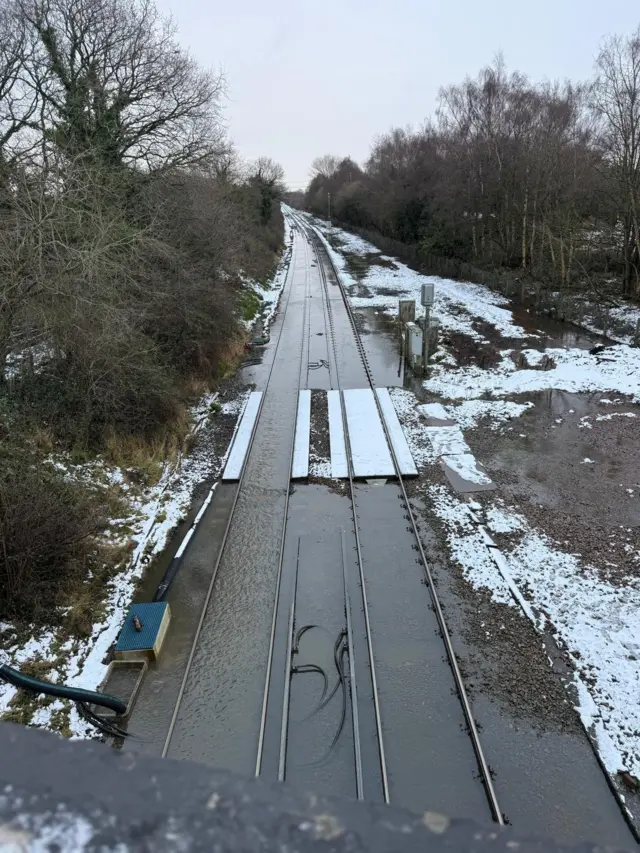 A photograph of flooded railway lines taken from a railway bridge. Snow can be seen either side of the tracks