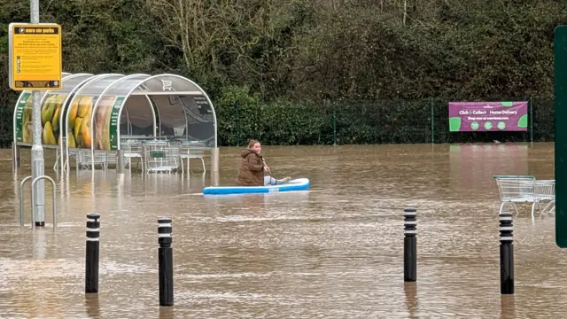 Shawna Mann sitting on a paddleboard as she floats around a submerged supermarket car park