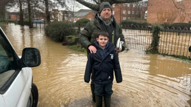 Man and child standing wearing wellies in flood