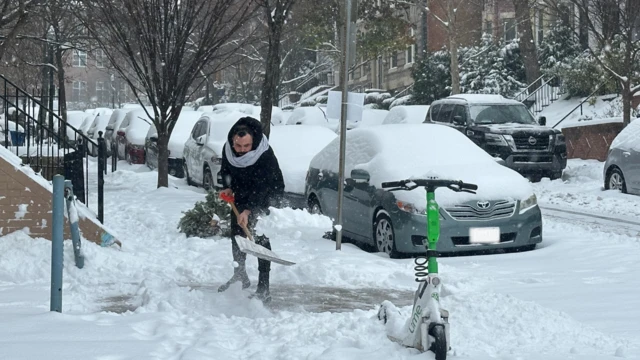 A man shovels snow in Washington, as cars and a scooter covered in snow