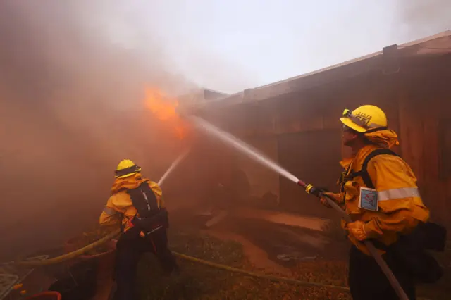 Firefighters work to extinguish flames engulfing a home as a brush fire rages in Pacific Palisades, California