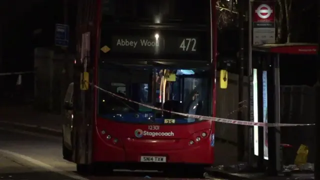 A 472 London bus is seen at night, and there is police tape cordoning it off.