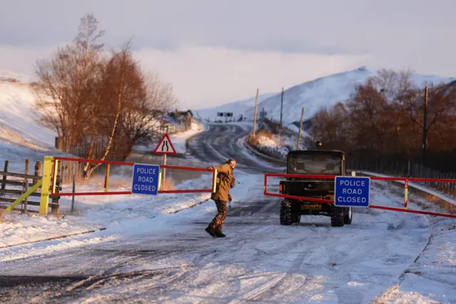 Snow gates are closed on the A93 near Glenshee. A man can be seen getting out of a vehicle and pulling two red gates together