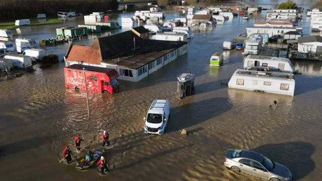 Rescue team guiding kayak with a person through flooded caravan park