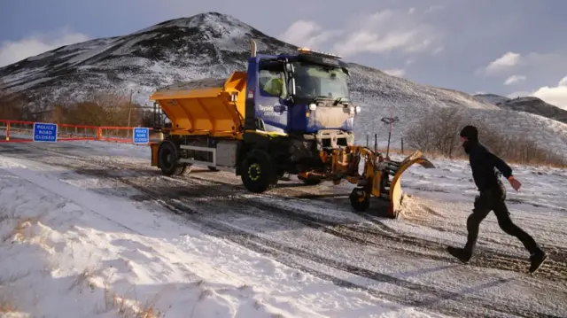 Gritter with mountain in the back and man clad in black