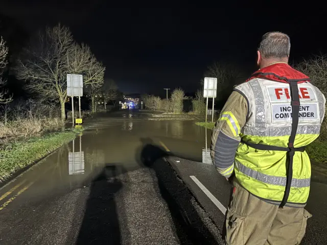 A firefighter looks on at a stranded vehicle in the distance