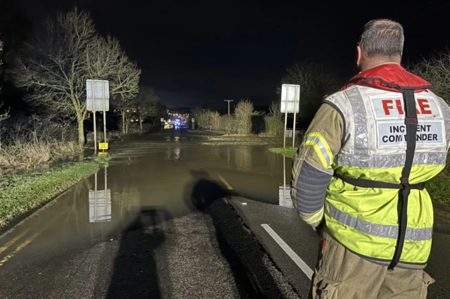 A firefighter looks down a country road where a person is being rescued from a trapped car as a result of rising flood waters