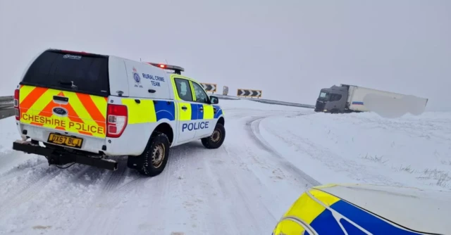 Two police cars on a snowy bend with a lorry stuck in the background