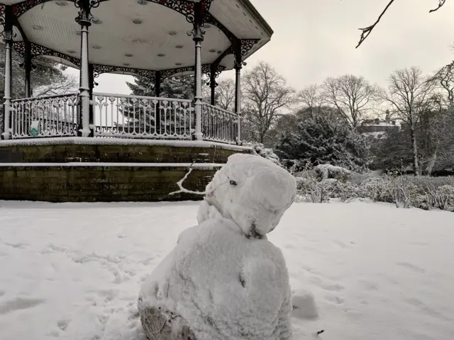 A snowman next to a bandstand in a snow laden park