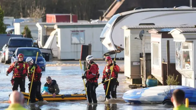 Rescue team kayaking a person through flooded caravan park