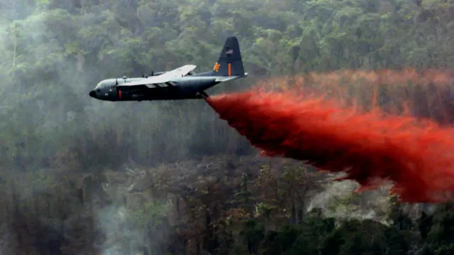 A US Air National Guard C-130 Hercules dropping red fire retardant on a forest fire