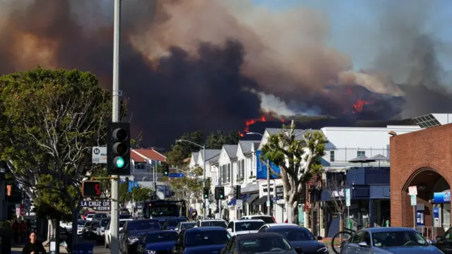 People evacuate, as smoke rises from a wildfire burning near Pacific Palisades on the west side of Los Angeles during a weather driven windstorm, in Los Angeles