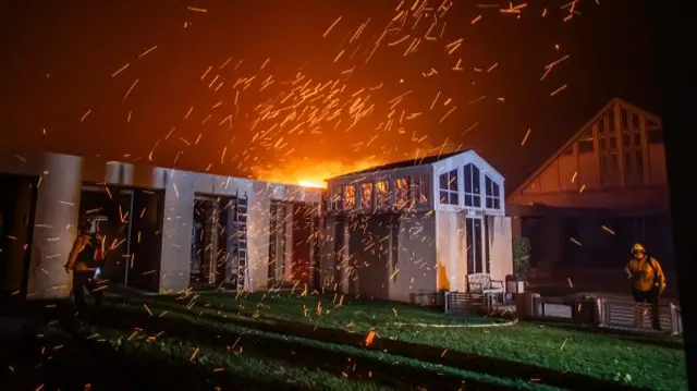 A firefighter watches the flames from the Palisades Fire burning in front of the Pacific Palisades Presbyterian Church during a powerful windstorm.