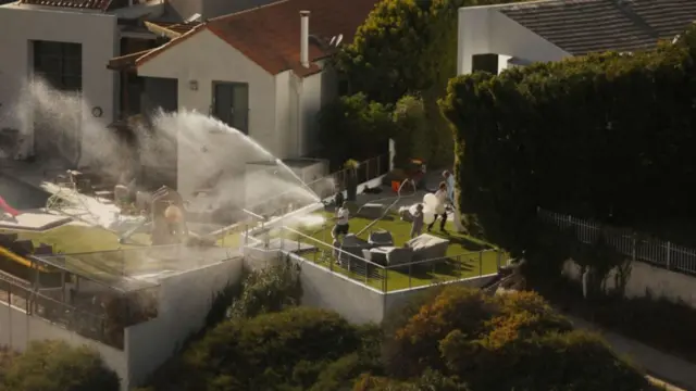 A man uses his hose to spray his property