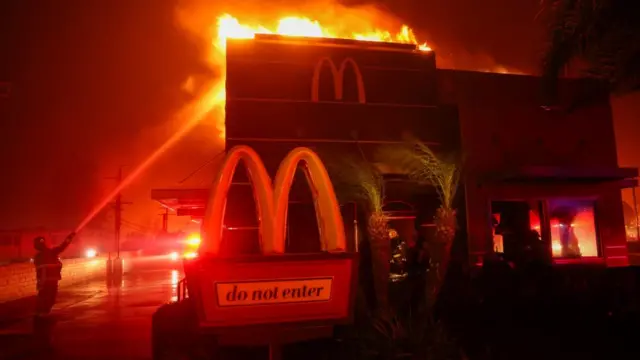 A firefighter tries to extinguish flames as a fire engulfs a McDonald's in Pasadena, California.