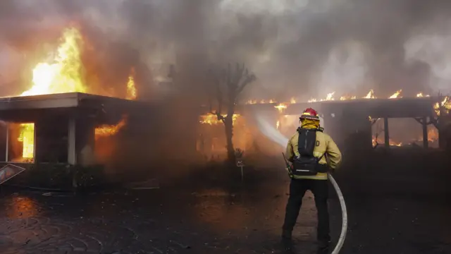 A firefighter uses a hose to battle a house fire