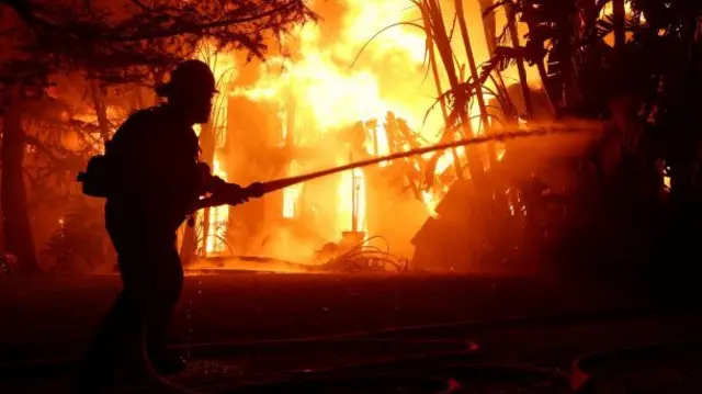 Los Angeles County firefighters spray water on a burning home as the Eaton Fire.