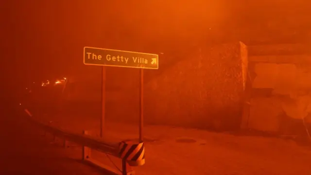 A sign pointing to the Getty Villa art museum in engulfed in red smoke from the flames of the wind-driven Palisades Fire in Pacific Palisades on 7 January