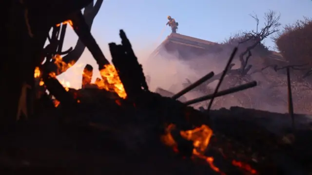 A firefighter douses a hot spot as a brush fire burns in Pacific Palisades