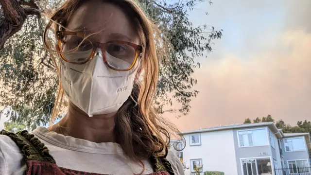 Lucy Sheriff seen wearing a mask with plumes of smoke in the background