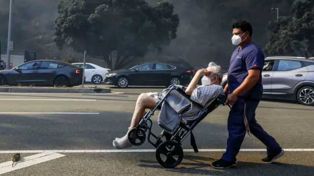 A man in a wheelchair is evacuated from a neighborhood being threatened by the Palisades wildfire