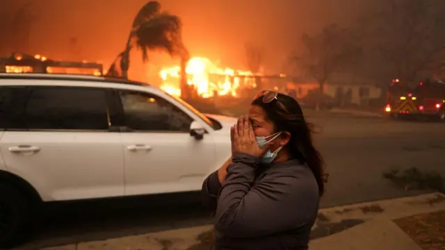 A woman reacts as she evacuates following powerful winds fuelling wildfires in the Los Angeles area, at the Eaton Fire in Altadena, California