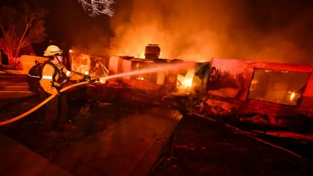 A firefighter from Costa Mesa works to extinguish a fire burning a home on Valleylights Drive during the Eaton fire in the Hastings Ranch community of Pasadena early Wednesday morning