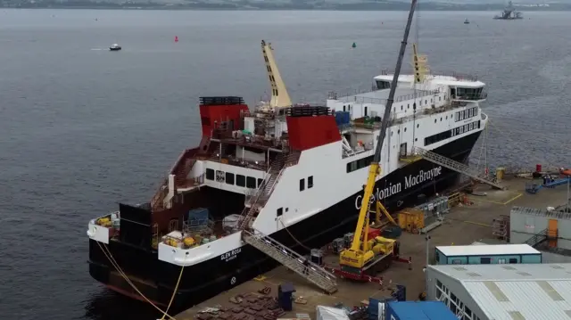 A large black and white ship at a dock with a large yellow crane beside it