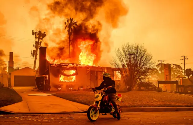 A motorcyclist stops to look at a burning home during the Eaton fire in Altadena.