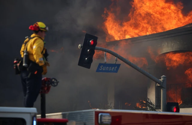 A firefighter stands facing fire flames, as powerful winds fueling devastating wildfires in the Los Angeles area force people to evacuate, in the Pacific Palisades neighborhood on the west side of Los Angeles