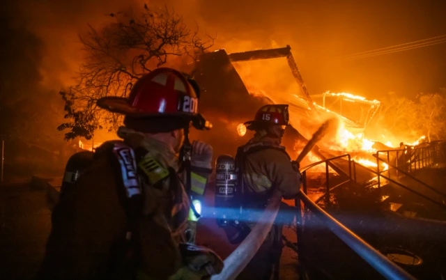 Firefighters fight the flames from the Palisades Fire burning the Theatre Palisades during a powerful windstorm