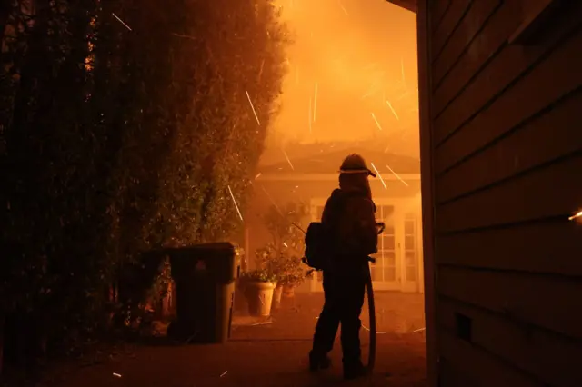 A firefighter battles Palisades blaze near a home