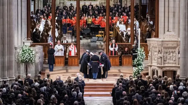 The casket being placed on a stand at the front of the cathedral