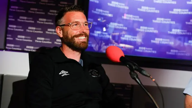 Rob Edwards sitting in the studio at BBC Three Counties Radio. He is smiling in front of a microphone.